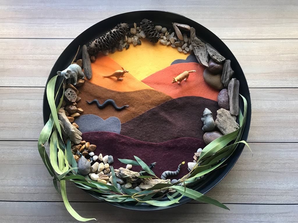 A small world play tray set up using a bunnings plant saucer, a handmade felt mat and some natural loose parts such as stones, seed pods, driftwood, and natural gum leaves, featuring  our wild republic Australian  nature tube. 